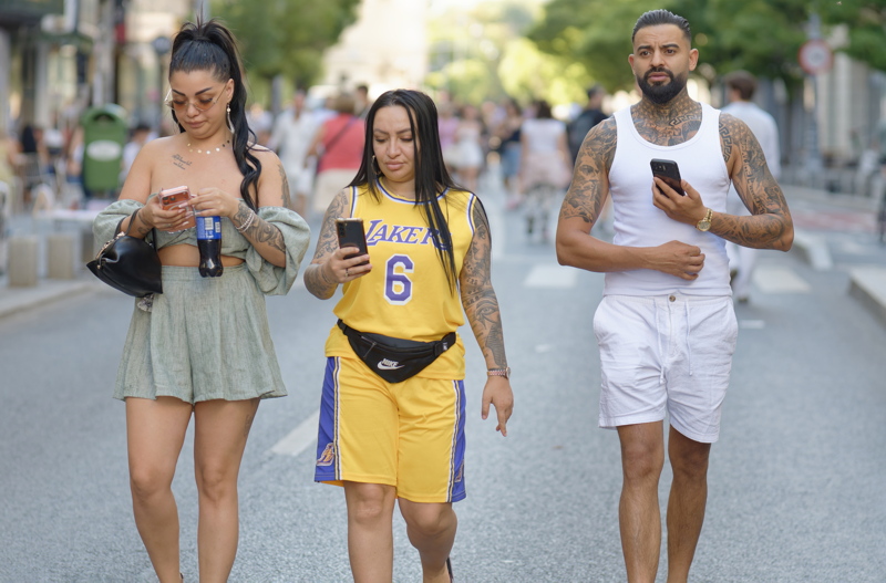 6 - Three individuals walking down a street, with the central figure wearing a yellow Los Angeles Lakers jersey